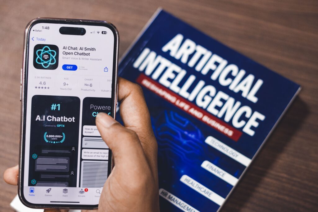 Ruka drží smartfón s aplikáciou AI chatbot GPT pre písanie esejí vedľa knihy Artificial Intelligence